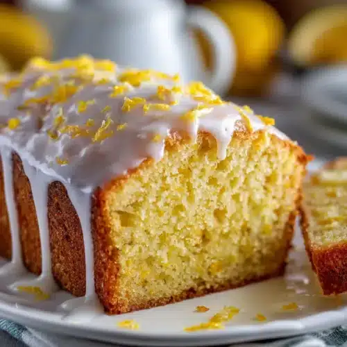 Thick slices of lemon loaf cake with lemon glaze, fresh zest, and raspberries on a rustic board