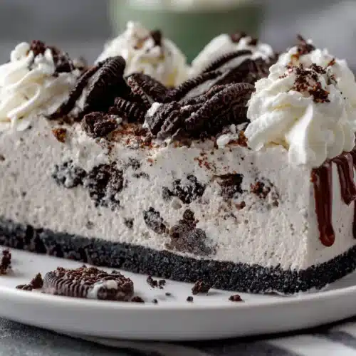 No bake cookies and cream mousse cake with layers of fluffy mousse and Oreo cookie crust, topped with whipped cream and cookie crumbles.