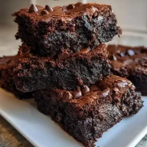 Delicious chocolate dessert squares on a plate, topped with chocolate drizzle.